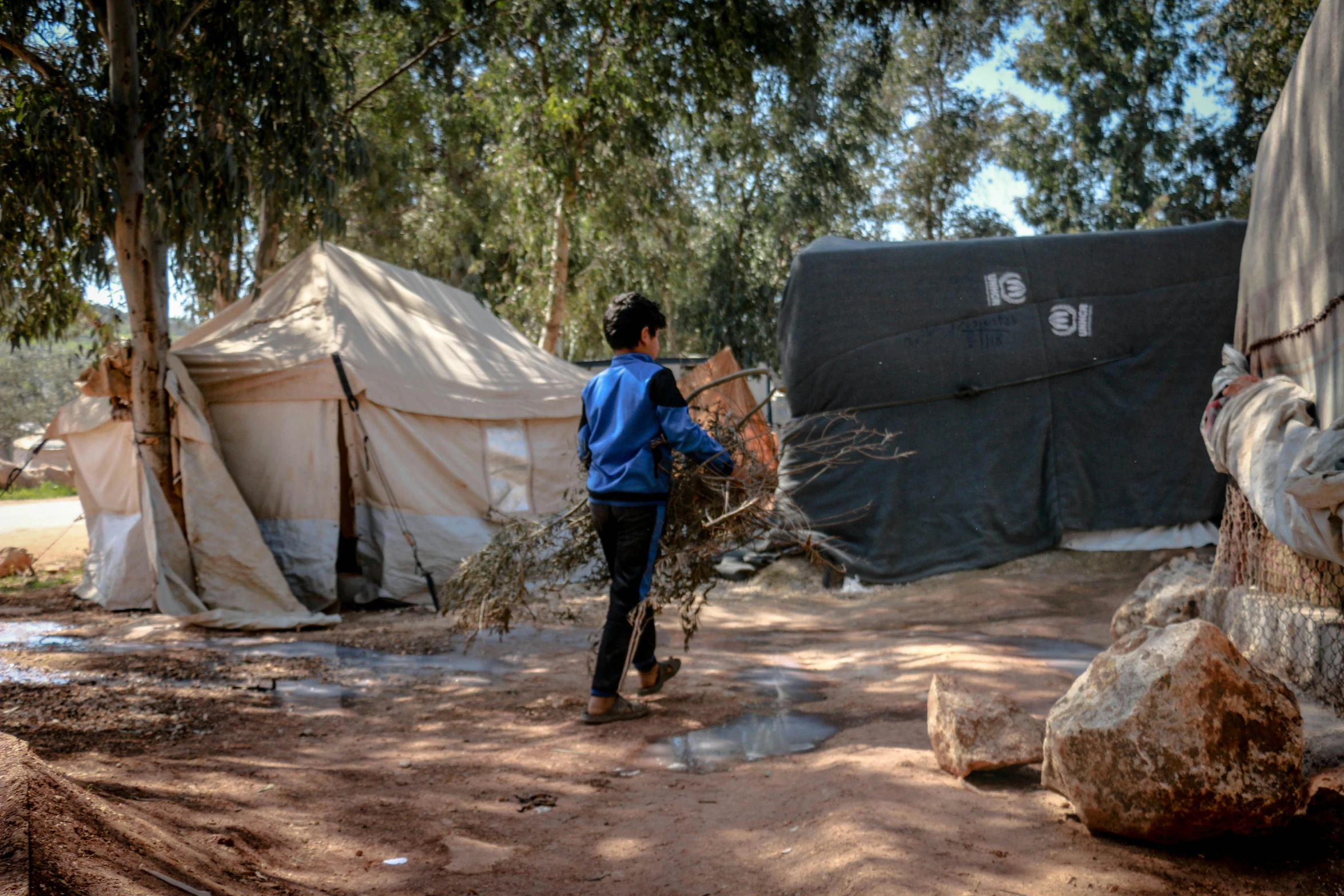 a person that is standing in the dirt, by Julia Pishtar, hurufiyya, tents, teenage boy, dragging a pile of chains, olive trees