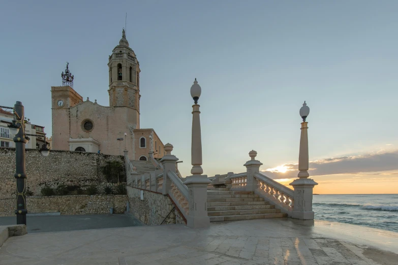 a clock tower sitting on the side of a building next to the ocean, a picture, inspired by Francisco Zúñiga, pexels contest winner, baroque, sunset panorama, steps, asymmetrical spires, monastery