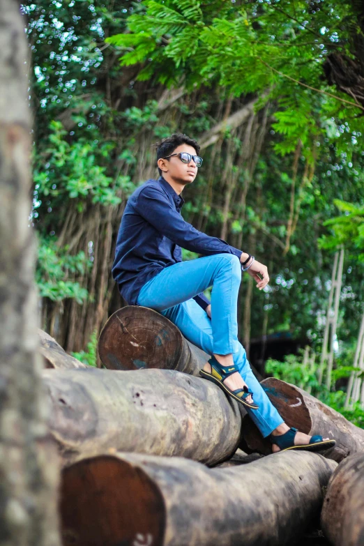 a woman sitting on top of a pile of logs, by Basuki Abdullah, handsome man, tight blue jeans and cool shoes, avatar image, portait image