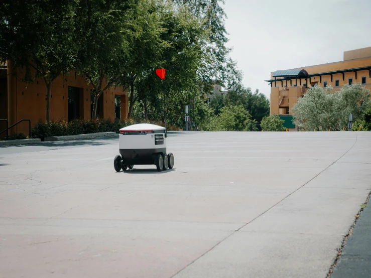 a robot in a parking lot with a red balloon in the background, delivering parsel box, on the concrete ground, josh grover, blurry