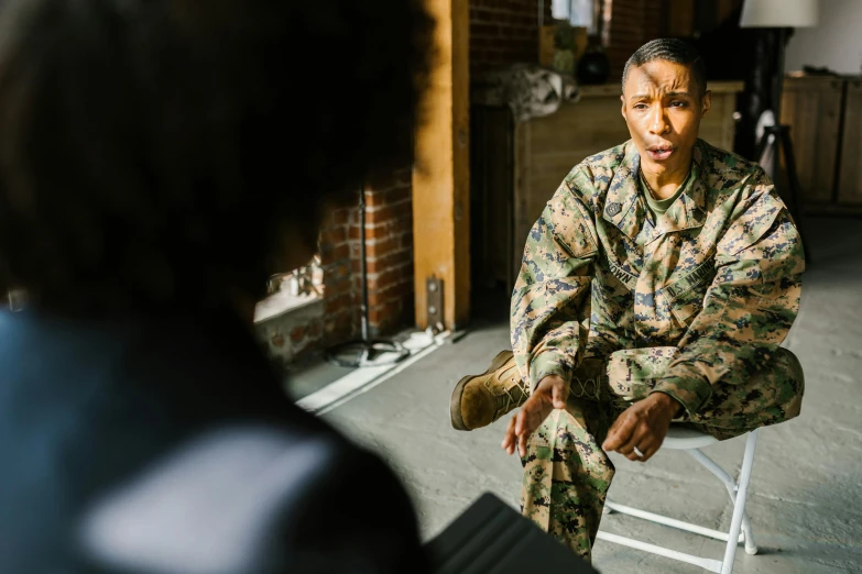 a woman in a military uniform sitting on a chair, pexels, giving an interview, ashteroth, ripped up field fatigues, male and female