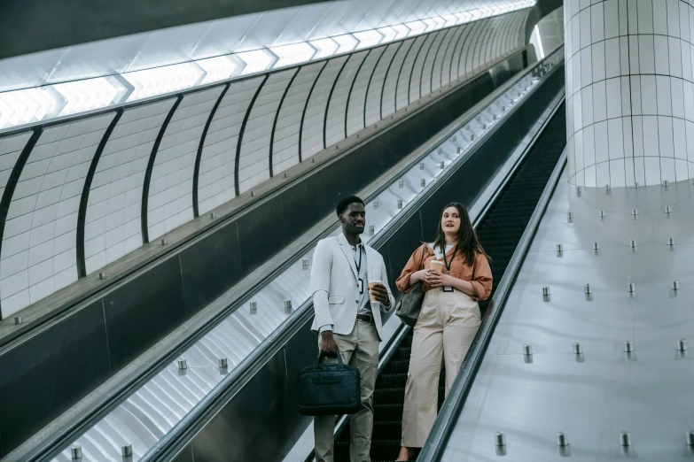 a couple of people standing next to each other on an escalator, by Emma Andijewska, pexels contest winner, happening, walking to work, underground facility, varying ethnicities, thumbnail