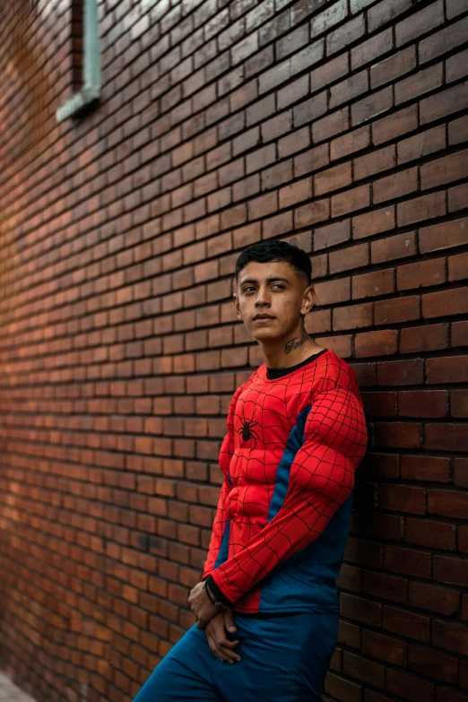 a man in a spider - man suit leaning against a brick wall, inspired by Carlos Berlanga, pexels contest winner, hyperrealism, 14 yo berber boy, very muscly, eloy morales, humans of new york