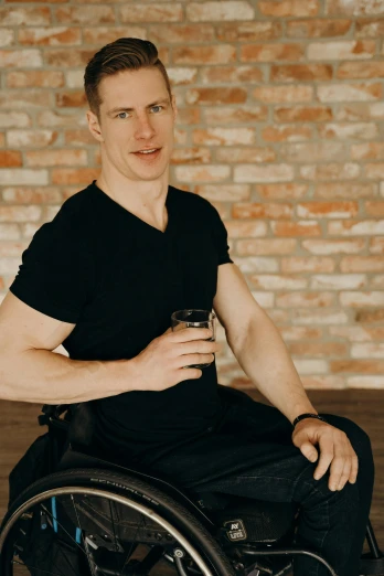 man with black shirt sitting in wheelchair with drink in hand