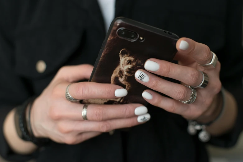 a close up of a person holding a cell phone, inspired by Elsa Bleda, trending on pexels, photorealism, runic rings, white and black, bears, nail art