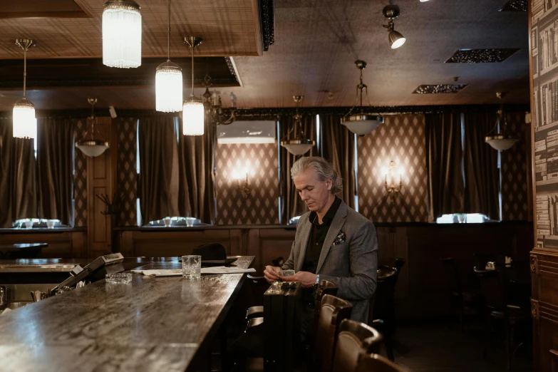 a man sitting at a table in a restaurant, by Dan Frazier, happening, gray haired, ignant, standing elegantly, sitting alone at a bar