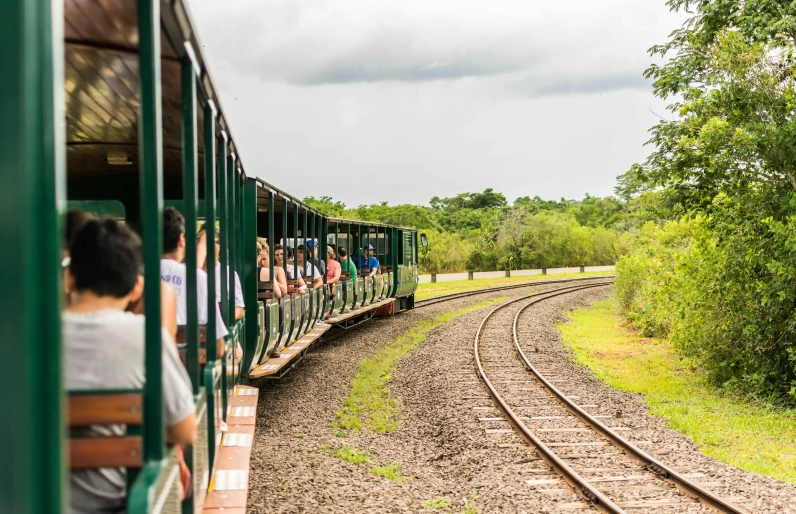passengers ride on the front and side of a small train as it rides down the tracks