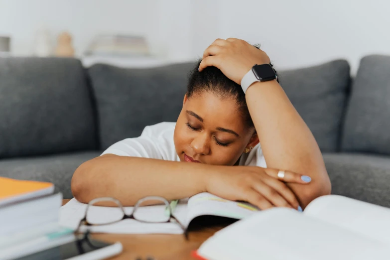 a woman sitting at a table with her head in her hands, pexels contest winner, happening, curled up on a book, snoring, black teenage girl, nursing