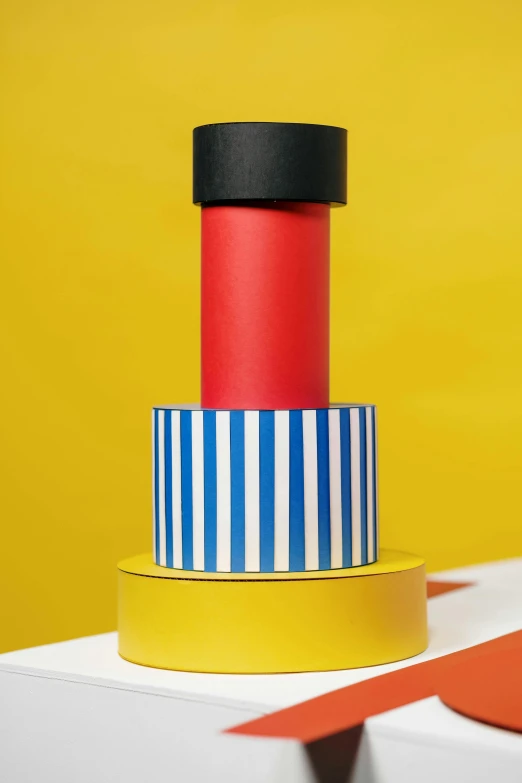 a red and blue cake sitting on top of a table, an abstract sculpture, inspired by Bauhaus, unsplash, de stijl, wearing cylinder hat, on yellow paper, lighthouse, profile close-up view