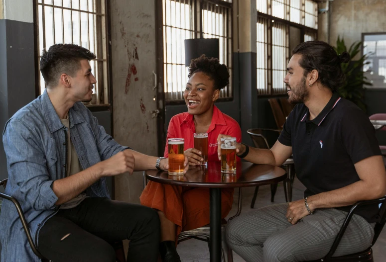 a group of people sitting around a table with beers, on a table, lgbtq, promotional image, portrait image