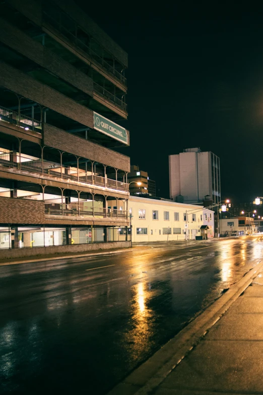 a city street at night with buildings in the background, brutalism, quebec, high-quality photo, ultrawide image, rainy