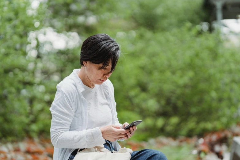 a woman sitting on a bench looking at her phone, trending on pexels, happening, maggie cheung, in the garden, avatar image, busy