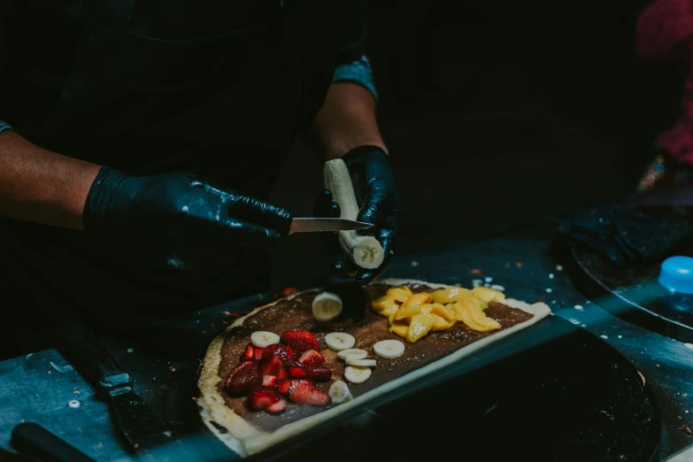 a person cutting a pizza with bananas and strawberries, by Daniel Lieske, pexels contest winner, wearing a dark hood, fully chocolate, aussie baristas, 1 7 8 0