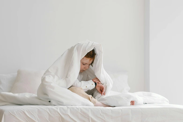 a woman sitting on top of a bed under a blanket, pexels contest winner, with a kid, white cloak, very tired, girl in raincoat