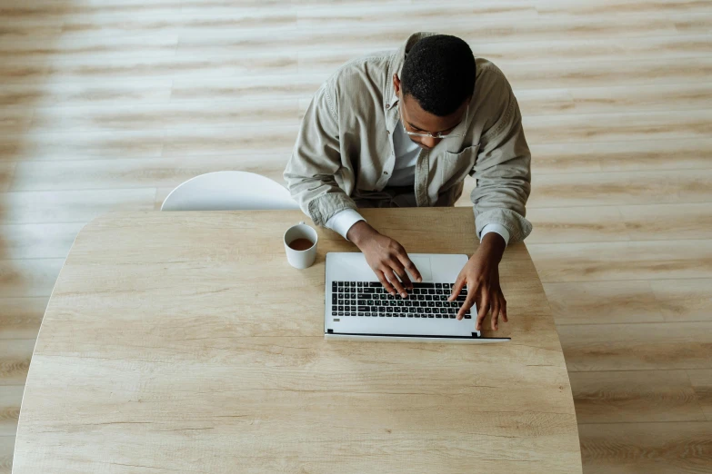 a man sitting at a table working on a laptop, by Carey Morris, pexels contest winner, sitting on a mocha-colored table, 1 4 9 3, riyahd cassiem, bottom angle