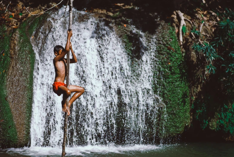 a man hanging from a rope in front of a waterfall, an album cover, by Ibrahim Kodra, pexels contest winner, sumatraism, loincloth, kano), kids, avatar image