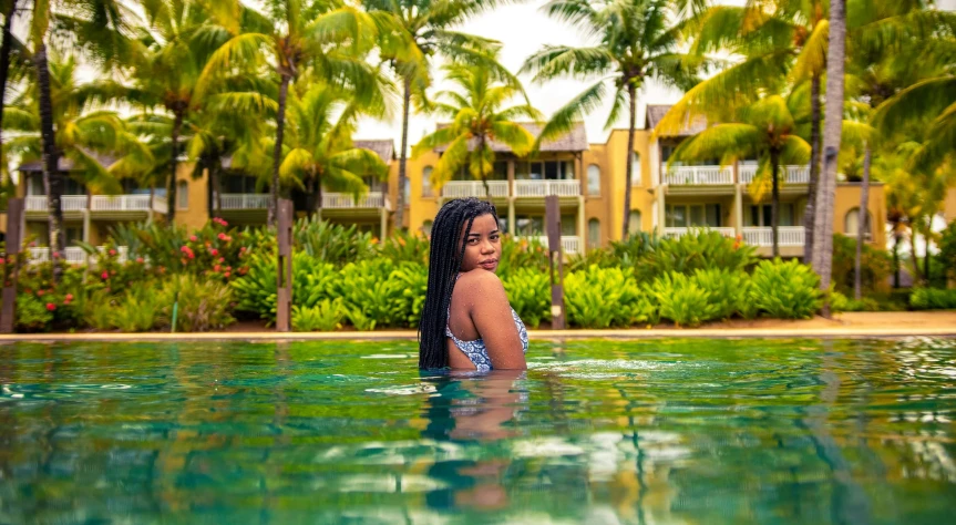 the woman is standing in the pool near a tropical building