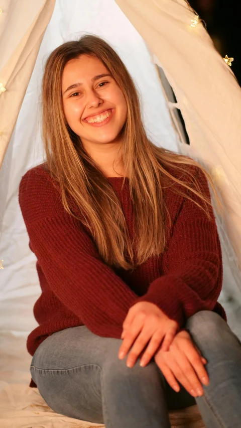 a beautiful young woman sitting in front of a teepee, pexels, red sweater and gray pants, very slightly smiling, official screenshot, environmental shot