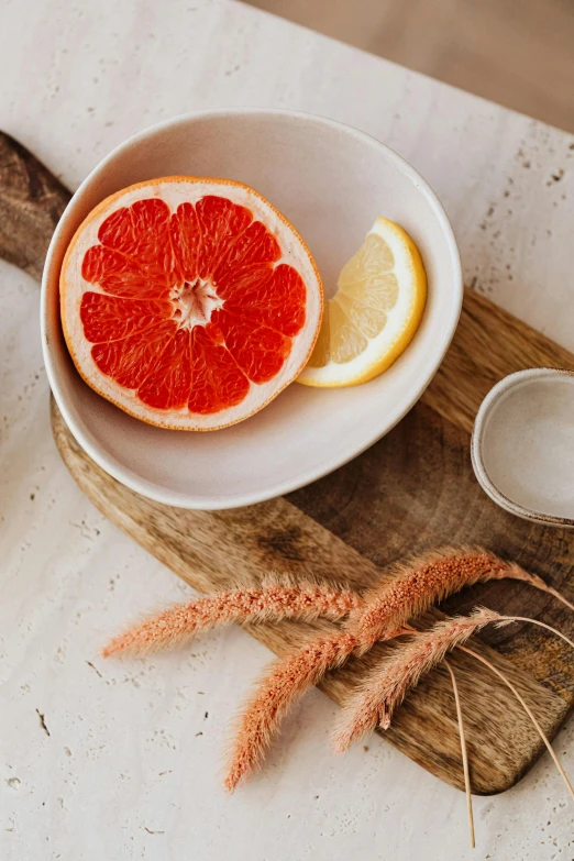 a bowl of fruit sitting on top of a wooden cutting board, coral, organic ceramic white, sliced grapefruit, subtle details