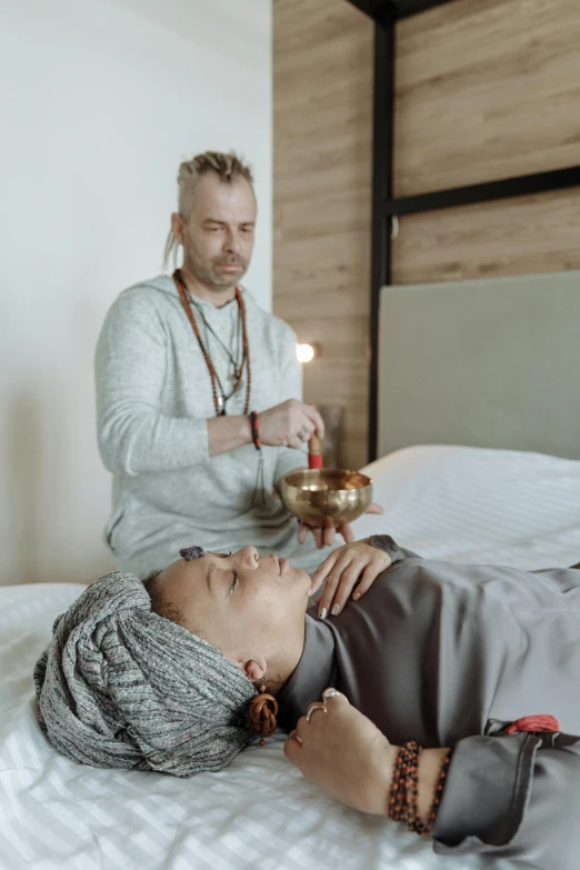 a woman laying on top of a bed next to a man, by Jan Tengnagel, trending on unsplash, renaissance, wearing long silver robes, health spa and meditation center, square, holding a bell