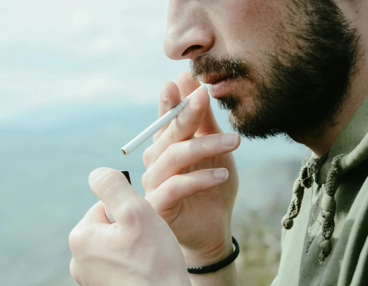 a man with a beard smoking a cigarette, trending on pexels, close up to a skinny, hemp, ultra - realistic, man