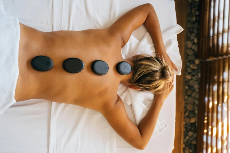 a woman laying on a bed with hot stones on her back, a mosaic, trending on pexels, in australia, black, arched back, indigo