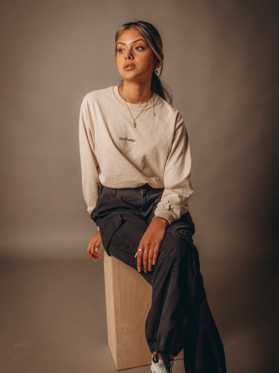 a woman sitting on top of a wooden box, outlive streetwear collection, cropped wide sleeve, natural muted tones, long sleeve