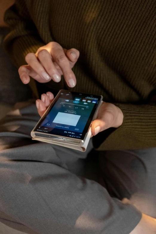 a close up of a person holding a cell phone, a picture, sitting on a bed, hammershøi, folded, large screen