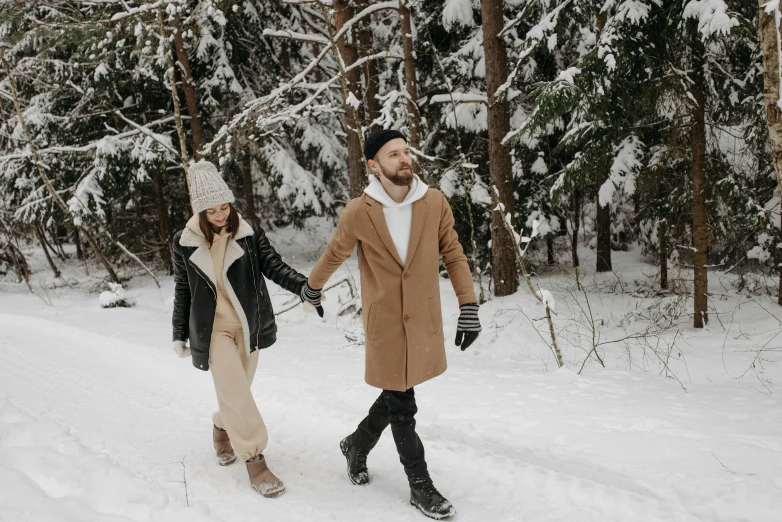 a man and a woman walking through the woods with snow on them