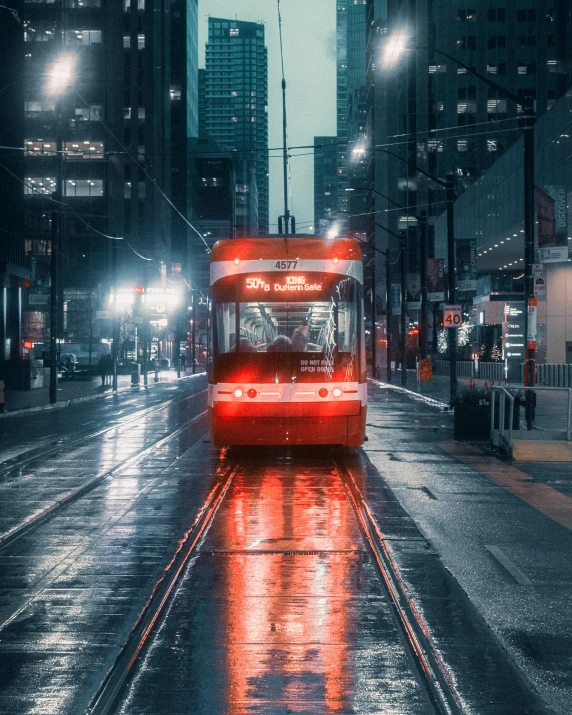 a red bus driving down a street next to tall buildings, an album cover, unsplash contest winner, rainy night, the city of toronto, tram, gif