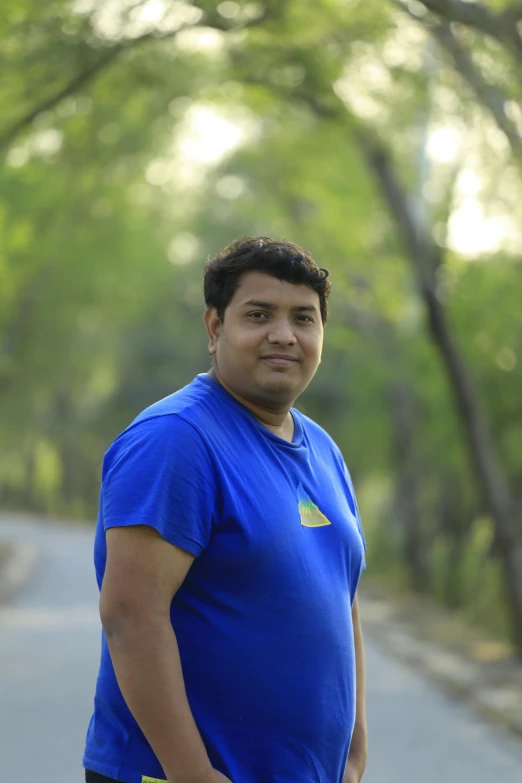 a man standing in the middle of a road, in front of a forest background, profile image, in blue and yellow clothes, desi