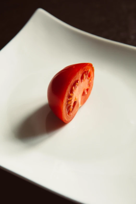 a tomato sitting on top of a white plate, ignant, half turned around, three quarter angle, medium angle