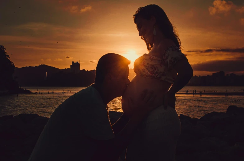 a man and woman standing next to each other near a body of water, a picture, by Elsa Bleda, pexels contest winner, maternity feeling, backlit sunset, profile pic, youtube thumbnail