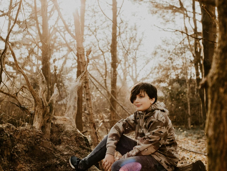 a woman sitting on a log in the woods, by Emma Andijewska, unsplash, portrait of 14 years old boy, wearing camo, non-binary, warm light