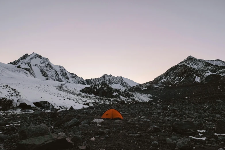 a tent pitched in a rocky area with mountains in the background, a picture, unsplash contest winner, postminimalism, orange glow, snowy mountains, 90s photo, gravel and scree ground