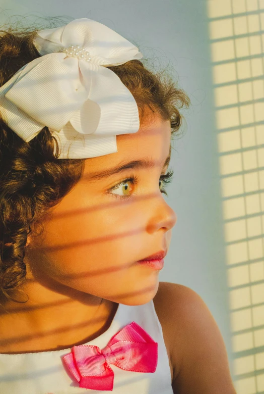 a little girl with a big bow on her head, an album cover, by Julian Allen, pexels contest winner, soft light through blinds, looking to the side, perfect crisp sunlight, heterochromia