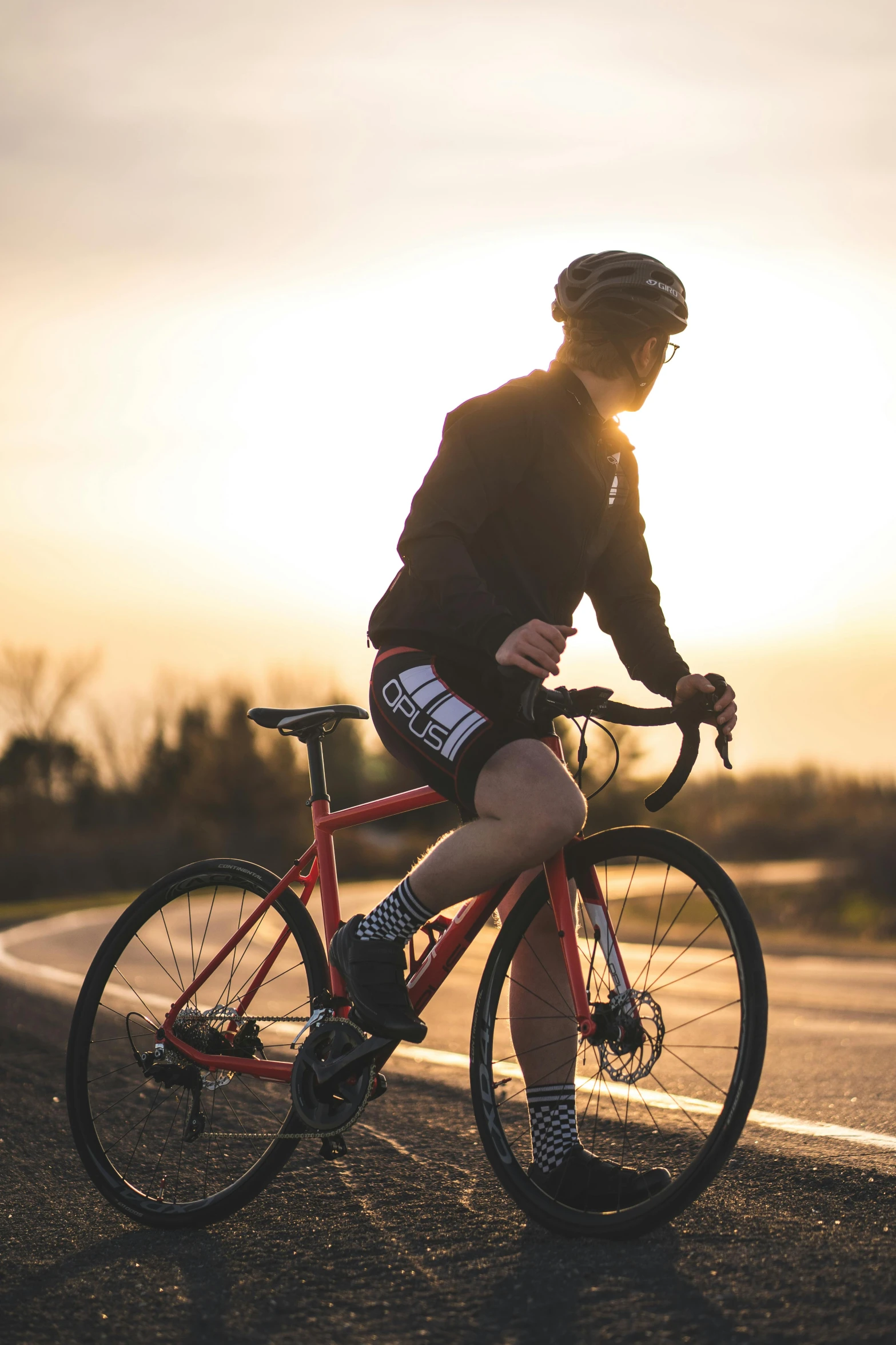 a man riding a bike on the side of a road, profile image, during a sunset, red sport clothing, kailee mandel