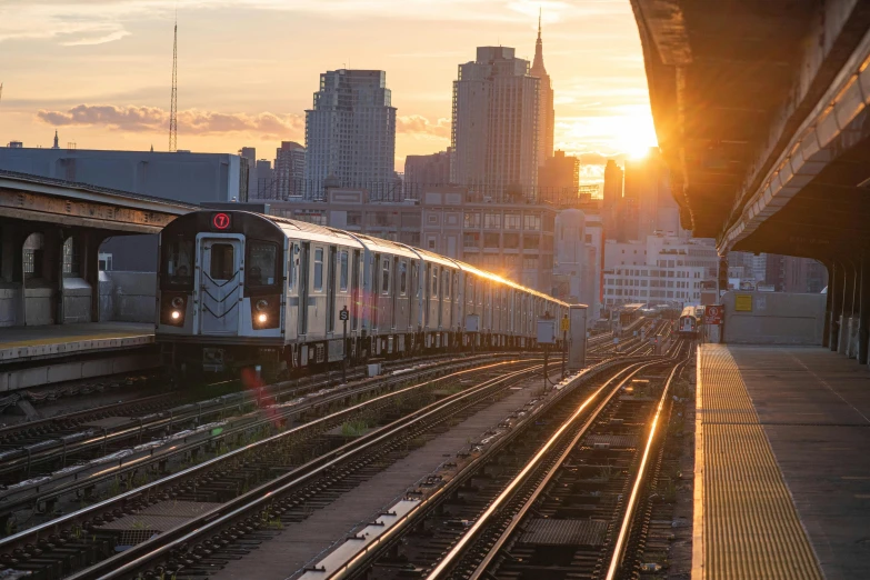 a train traveling down train tracks next to a train station, by Carey Morris, unsplash contest winner, golden hour in manhattan, skyline showing from the windows, 🚿🗝📝