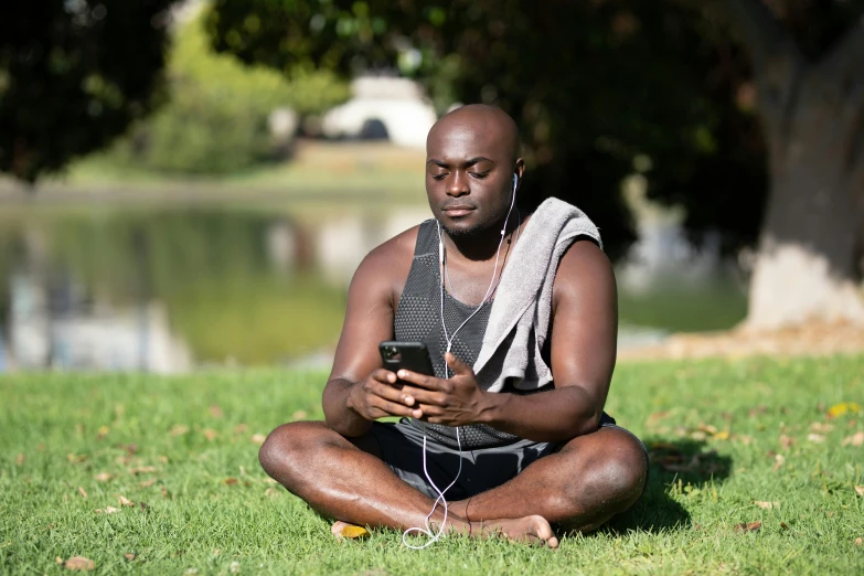 a man is sitting in the grass, while looking at his cell phone