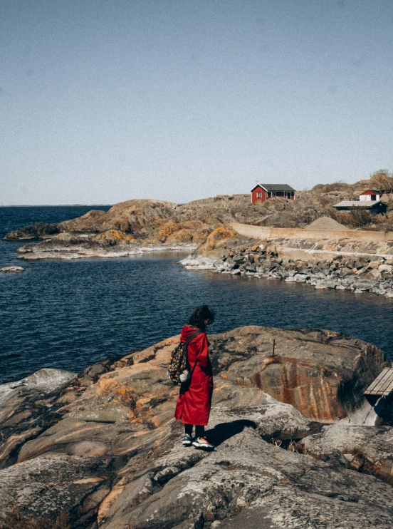 a person in a red dress standing on a rocky shore