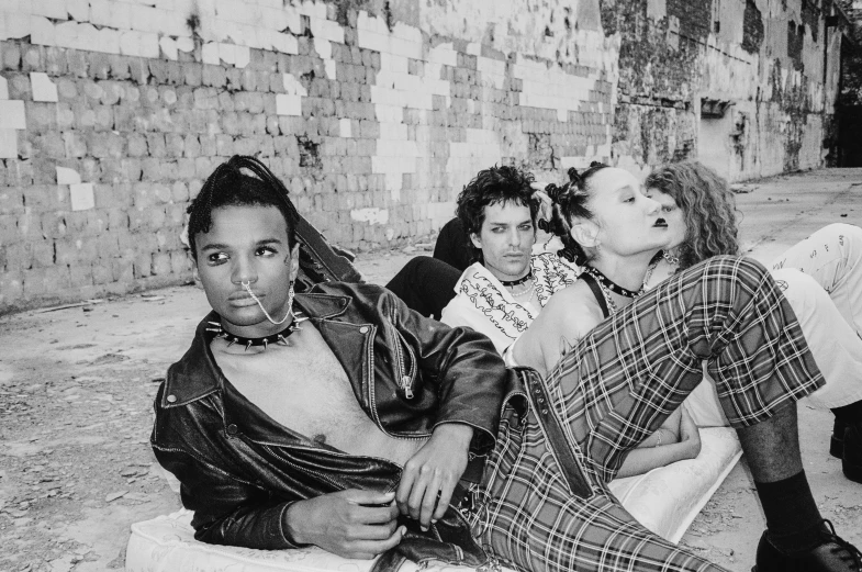 a group of people sitting next to each other, a black and white photo, renaissance, wearing a punk outfit, 80s hair, laying down, wearing studded leather