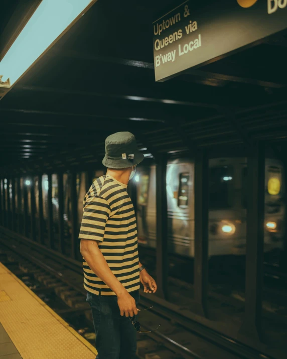 a man waiting for a train at a subway station, a polaroid photo, by Carey Morris, unsplash contest winner, lgbtq, stripes, wearing baseball cap, out in the dark