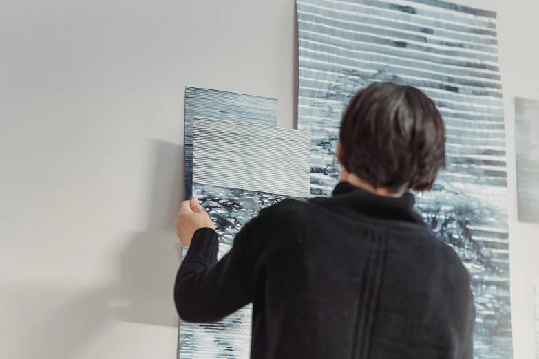 a woman standing in front of a painting on a wall, a photorealistic painting, inspired by Richter, unsplash, analytical art, shades of blue and grey, intricate ink painting detail, swiping brushwork, made in tones of white and grey