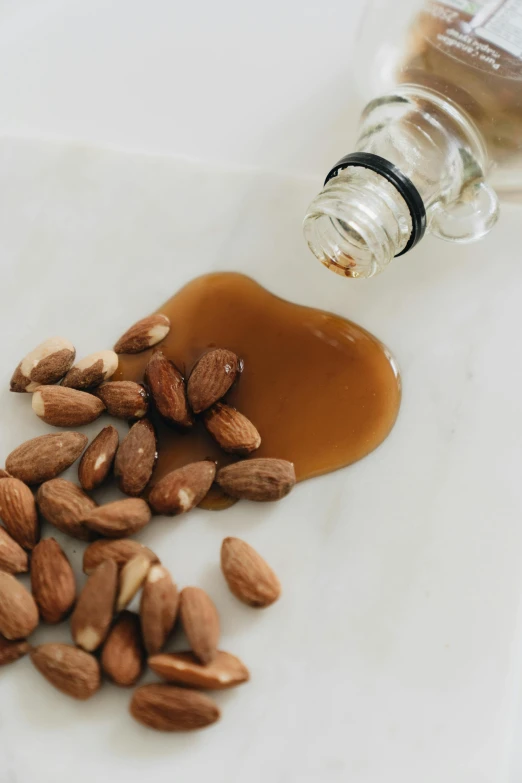 a bottle of syrup sitting next to a pile of almonds, by Jessie Algie, unsplash, renaissance, made of glazed, top down shot, panel, close-up product photo