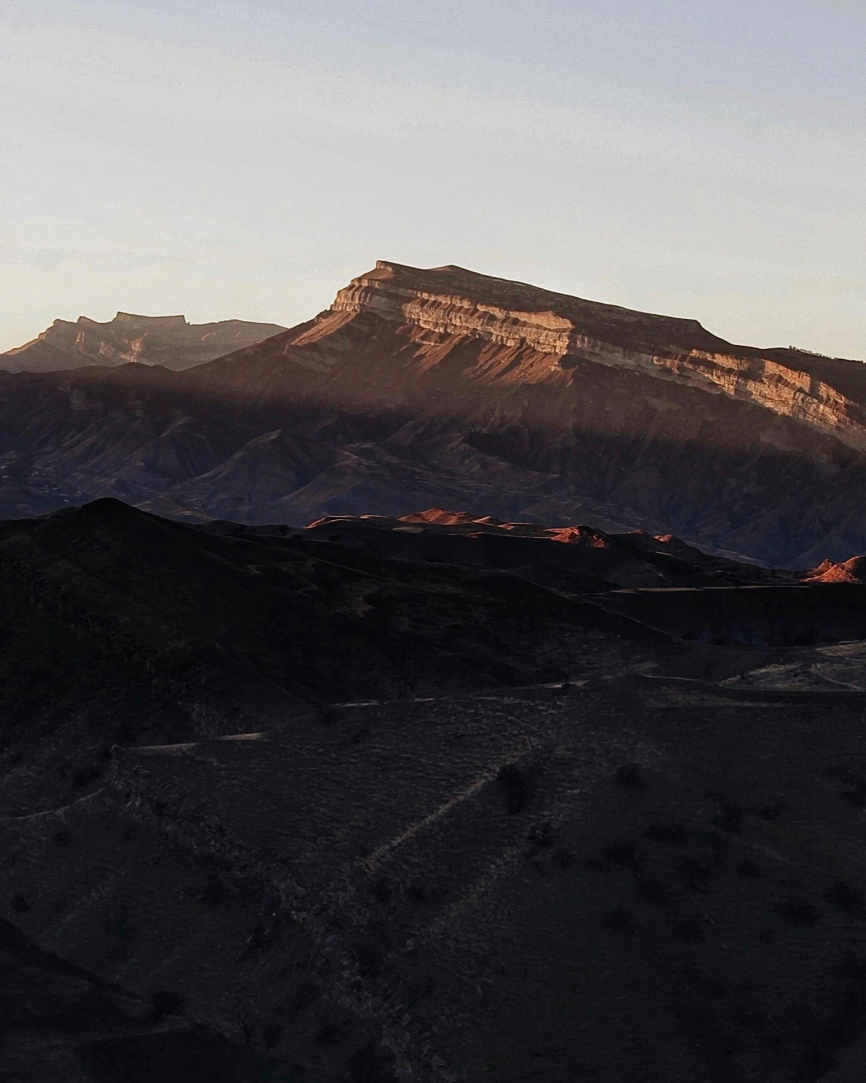 a mountain range at dusk with a distant peak