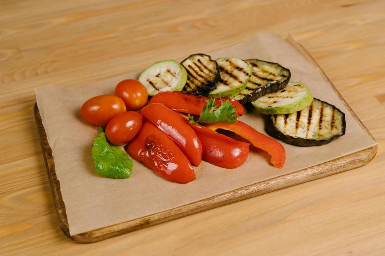 a cutting board topped with grilled vegetables on top of a wooden table, detailed product image, grey, parchment paper, full product shot