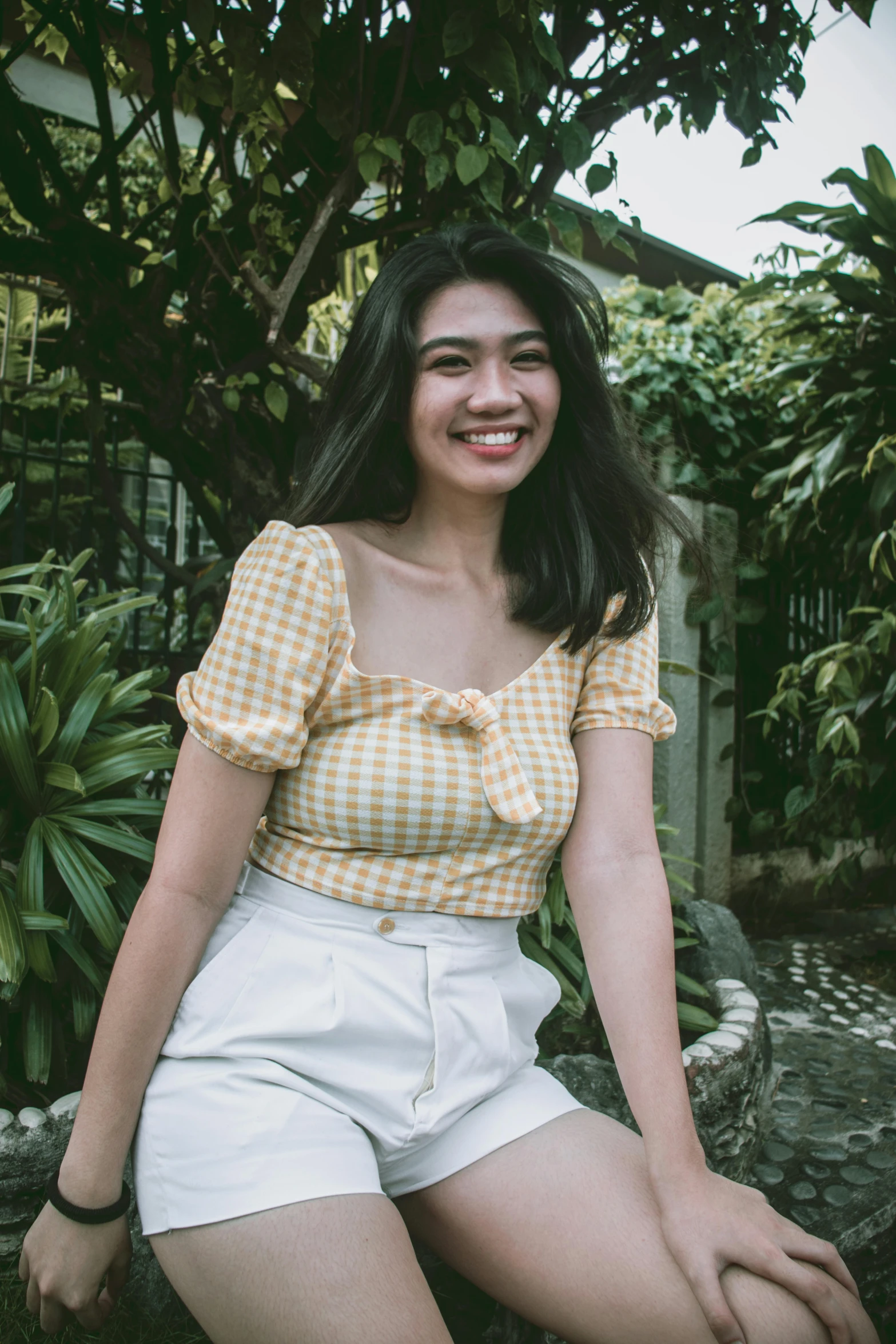 a woman sitting on a rock in a garden, inspired by Ruth Jên, pexels contest winner, happening, wearing yellow croptop, wearing a plaid shirt, manila, slight friendly smile