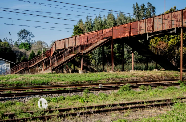 a train traveling down train tracks next to a bridge, by Peter Churcher, unsplash, graffiti, bent rusted iron, outdoor staircase, 1980s photo, mongezi ncaphayi