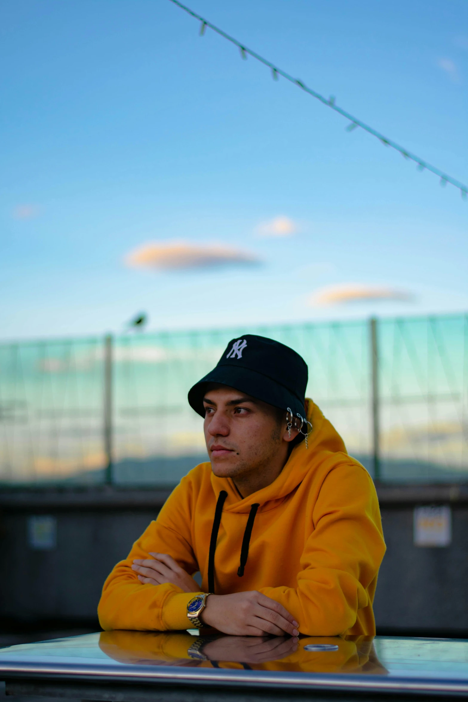 a man sitting at a table with his arms crossed, an album cover, unsplash, realism, yellow cap, skate park, headshot profile picture, skies