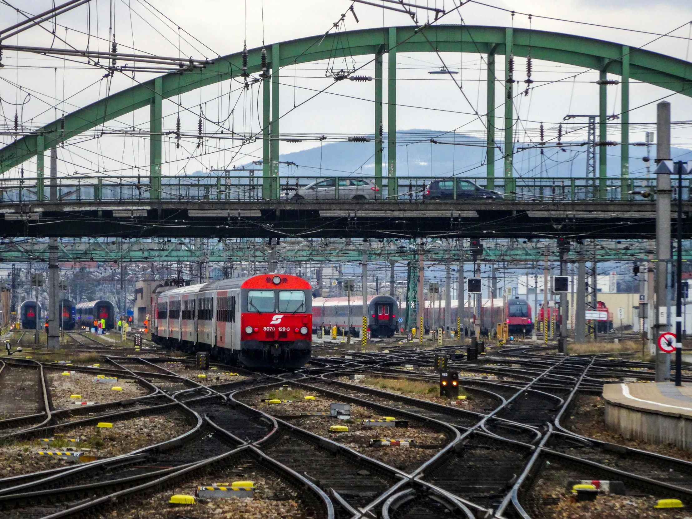 a red train traveling down train tracks under a bridge, a picture, by Tom Wänerstrand, terminals, photo of zurich, trains in the background, 🚿🗝📝